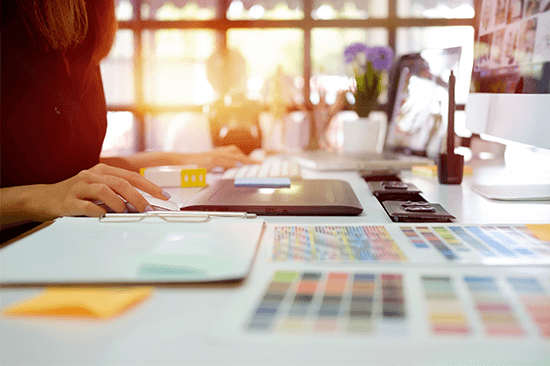 Eine Mediengestalterin vergleicht Farbwerte auf einem Farbfächer auf ihrem Schreibtisch